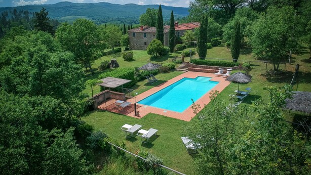 A rectangular swimming pool surrounded by a well-maintained lawn, with a stone building in the background and a mountainous landscape.