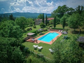 Une piscine rectangulaire entourée d’une pelouse bien entretenue, avec un bâtiment en pierre en arrière-plan et un paysage montagneux.