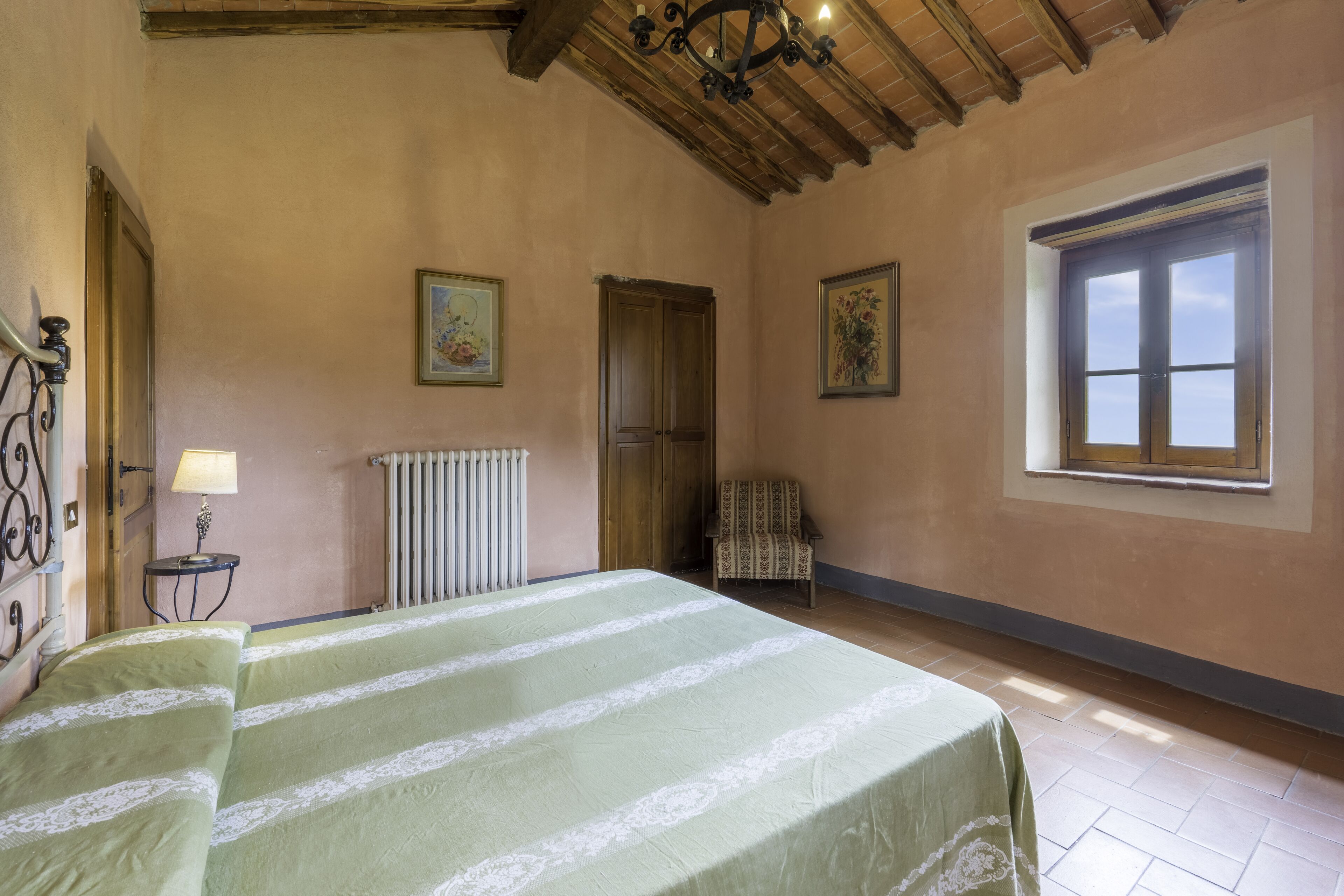 A bedroom with a bed, a chair, a radiator, and a window.