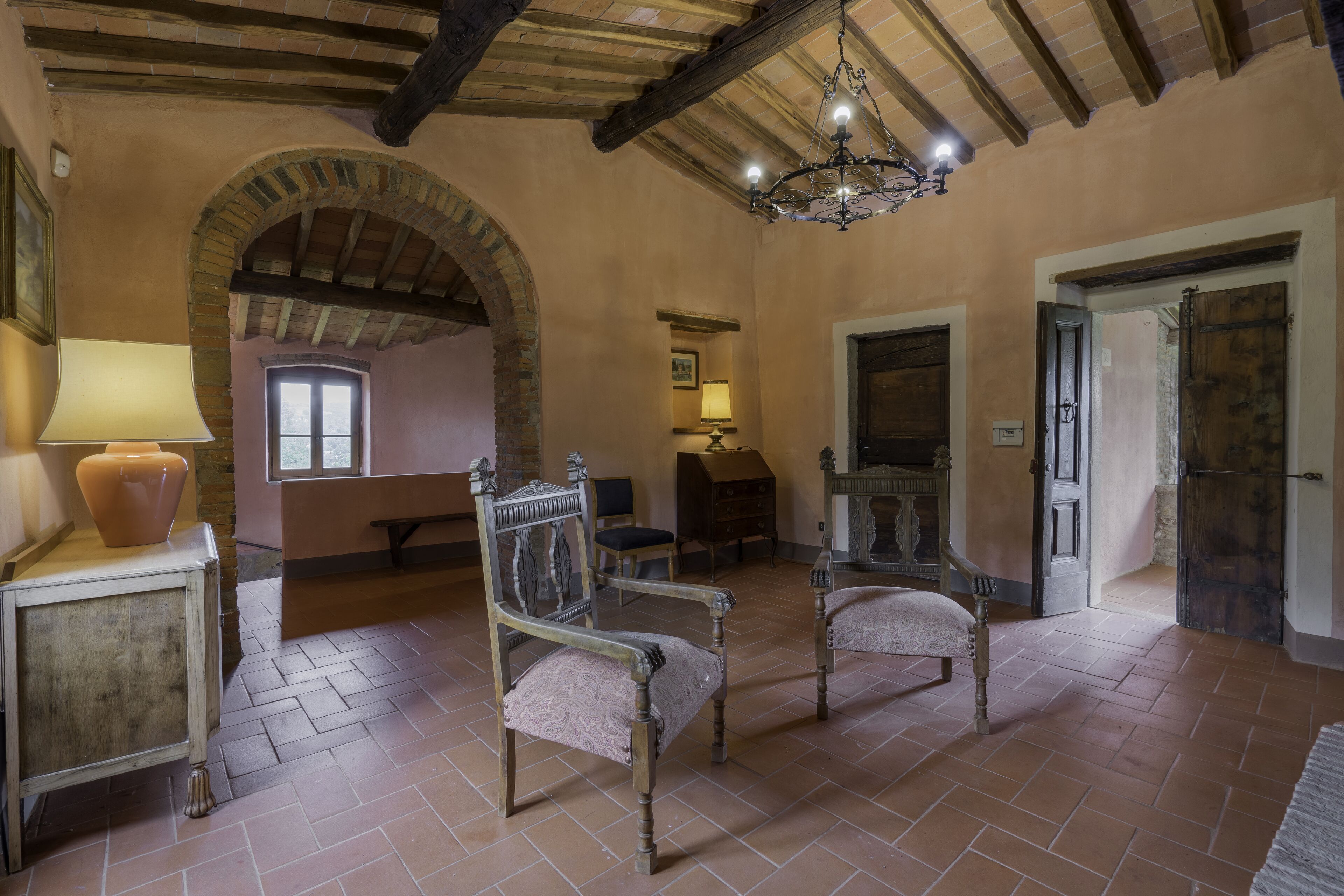 A room with a rustic interior, featuring exposed wooden beams, a chandelier, and a fireplace.