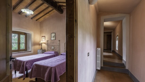 Una habitación con dos camas, una ventana, un radiador y una escalera que lleva a otra zona.