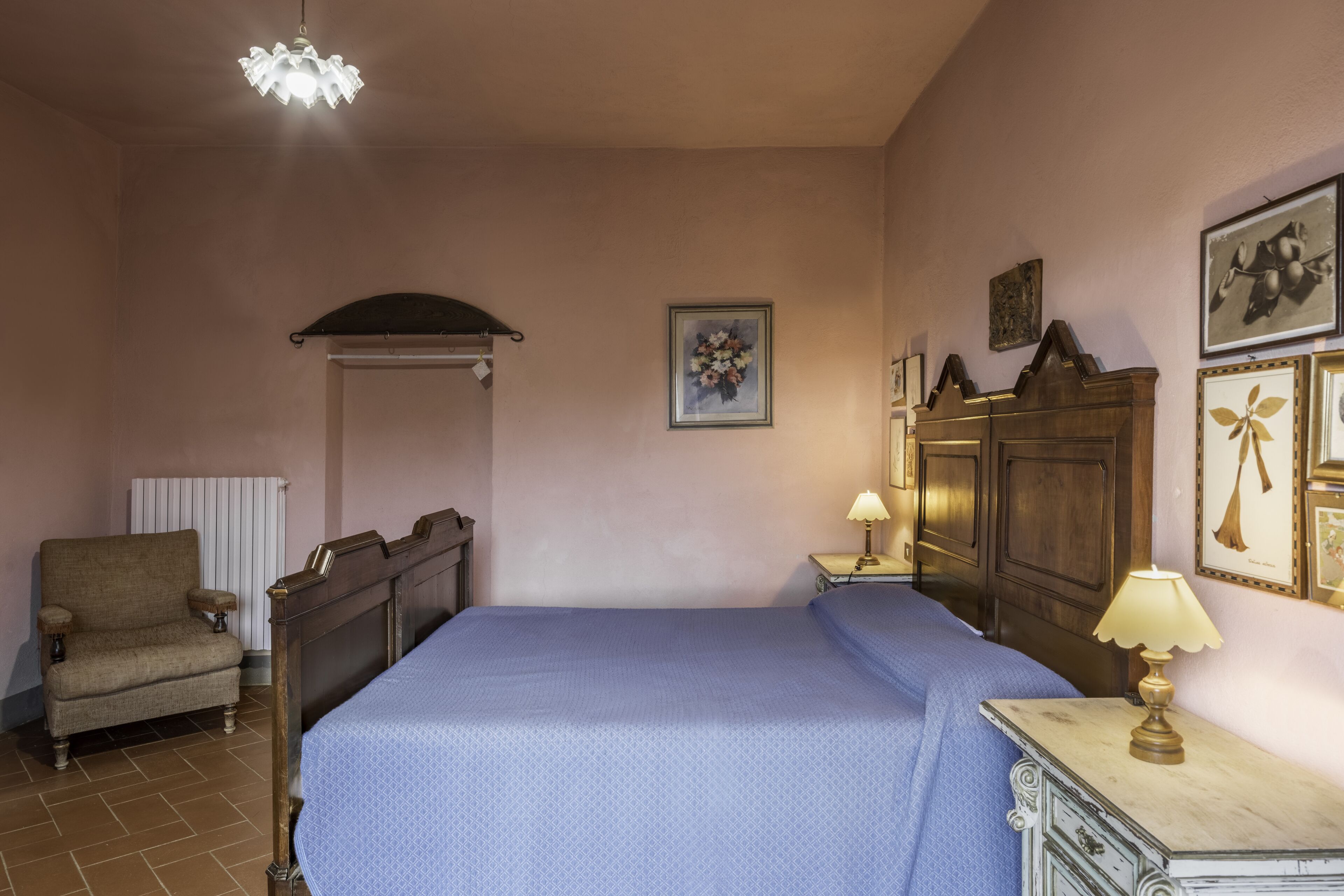 A bedroom with a bed, a chair, a nightstand, a lamp, and a radiator.