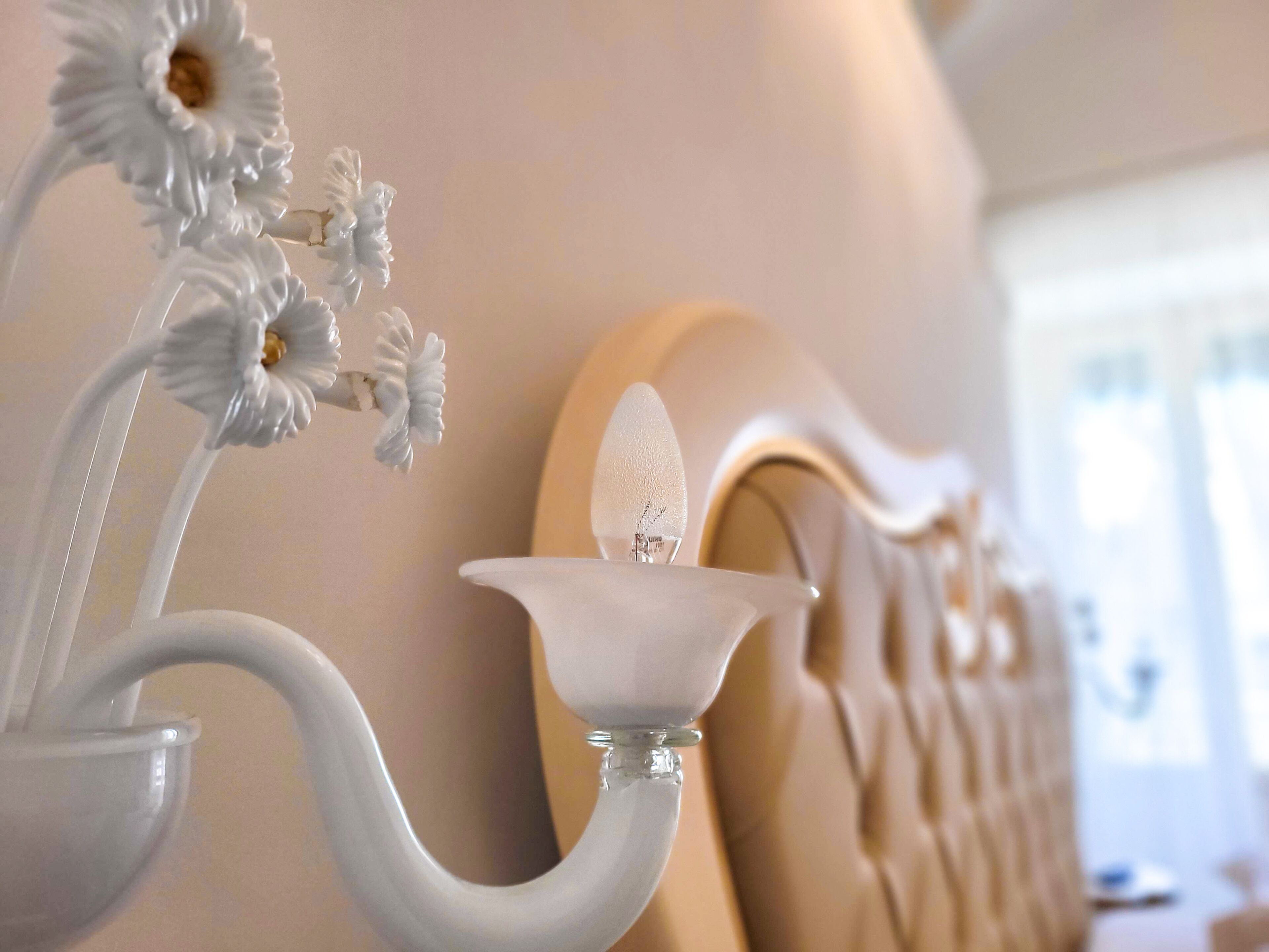 Un gros plan d’un appareil d’éclairage blanc, orné et fixé au mur, doté d’un abat-jour en verre et d’un motif floral.