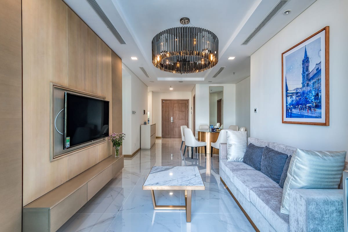 A modern living room with a flat-screen TV, a marble coffee table, a sofa, and a chandelier.