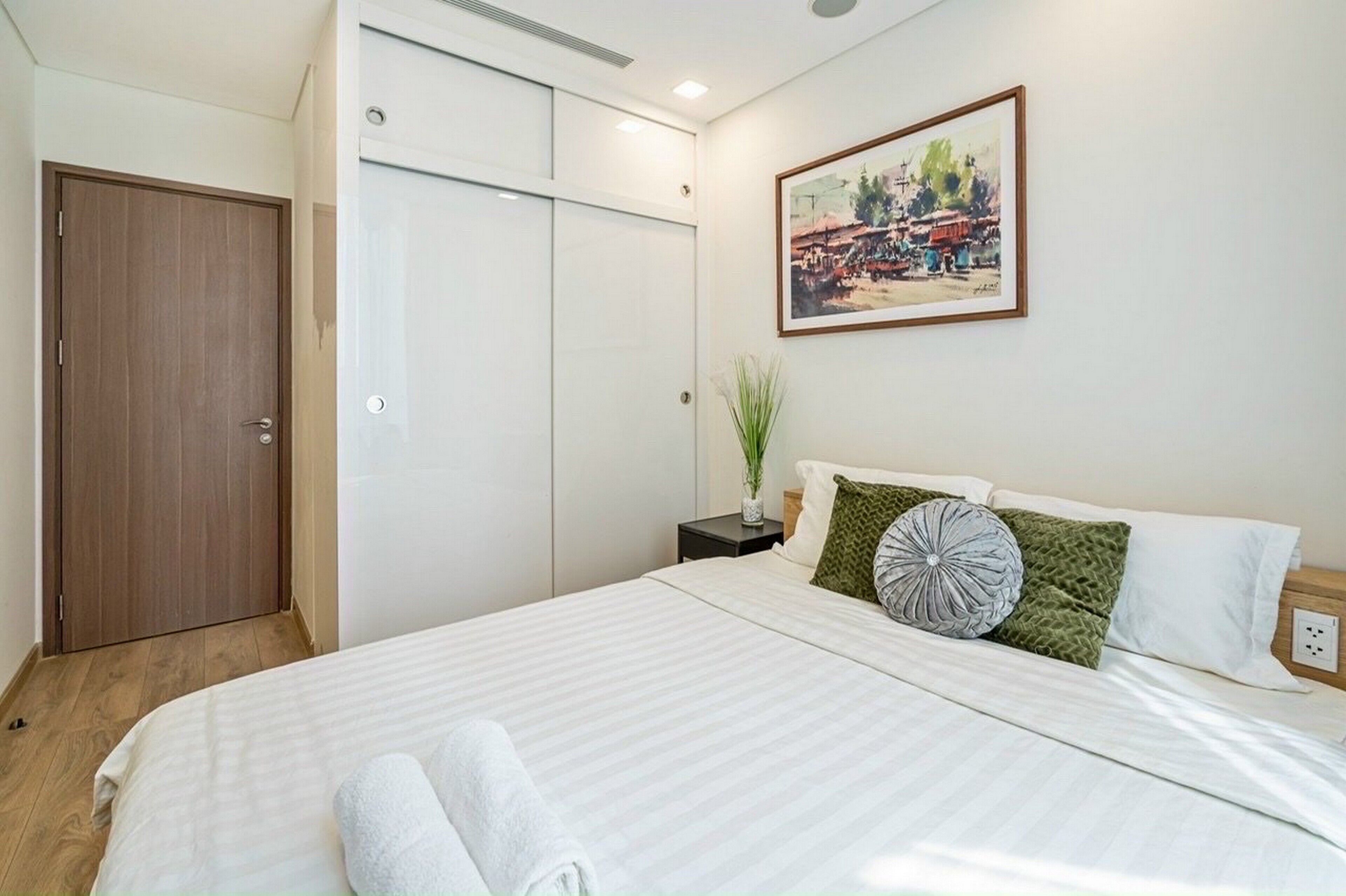 A bedroom with a bed, pillows, a nightstand, a painting, and a wardrobe.