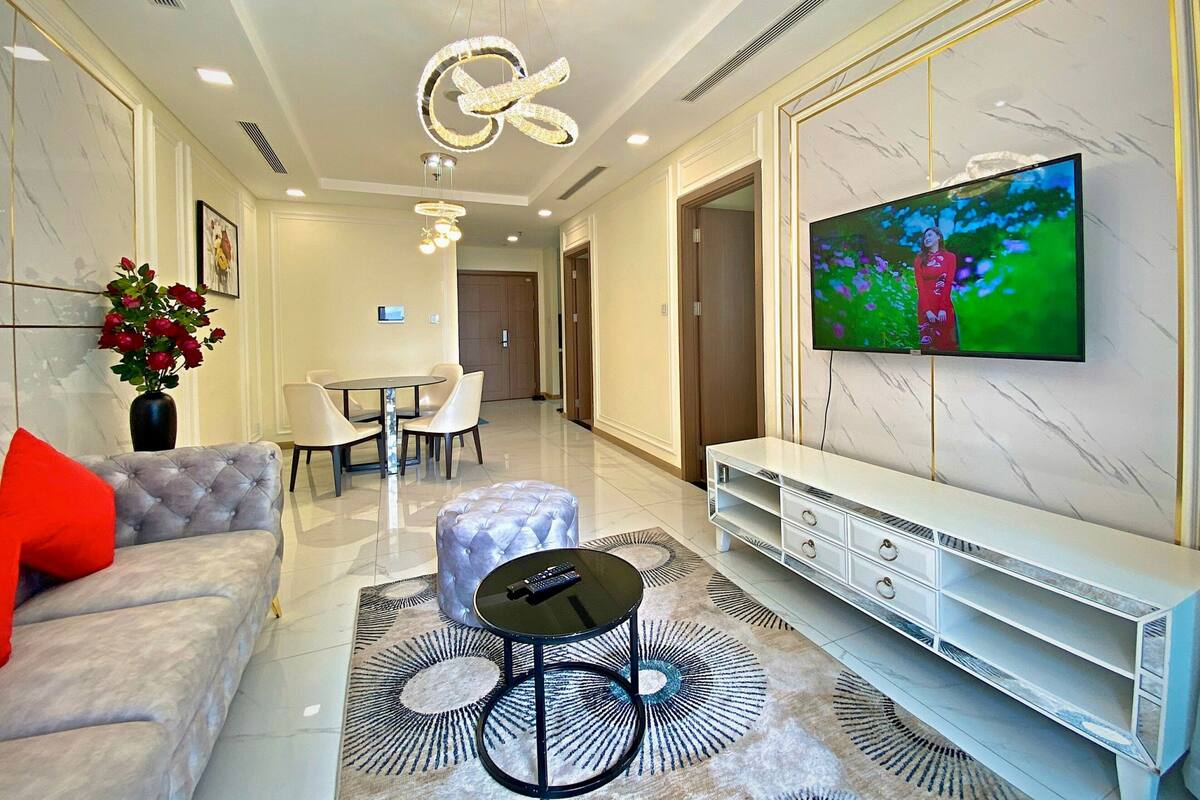 A modern living room with a marble wall, a flat-screen TV, a dining area, and a sofa with a red pillow.