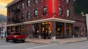 A multi-story building with a prominent neon sign, a fire escape, and a red vehicle parked in front.