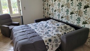 Quarto com cama, duas poltronas, janela, ar condicionado e parede com padrão de folhagem.