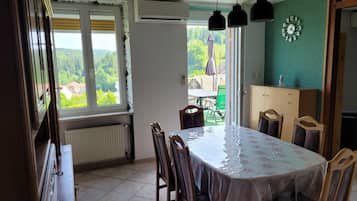 Un coin repas avec une table et des chaises, une vue par la fenêtre et une horloge au mur.