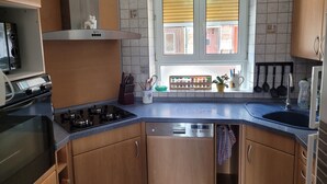 Uma cozinha com armários de madeira, fogão a gás, lava-louças e uma janela com persianas.