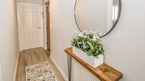 A hallway with a white door, a round mirror on the wall, and a white planter with flowers on a wooden console.