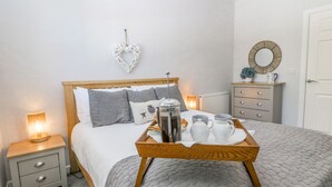 A neatly arranged bedroom with a bed, bedside tables, a dresser, and a tray with breakfast items.