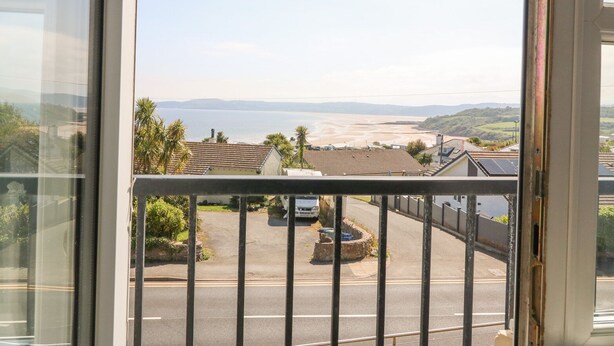 A view from a balcony overlooking a coastal area with a road, parked cars, and buildings.
