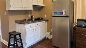 A kitchen with white cabinets, a stainless steel refrigerator, a coffee maker, and a trash can. -  Cozy room studio (Niagara Falls)