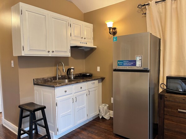 Una cocina con armarios blancos, un refrigerador de acero inoxidable, una cafetera y un cubo de basura.