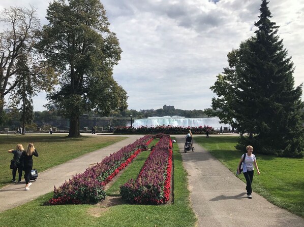 En park med en asfalterad gångväg, blomsterrabatter och ett vattenfall i bakgrunden.