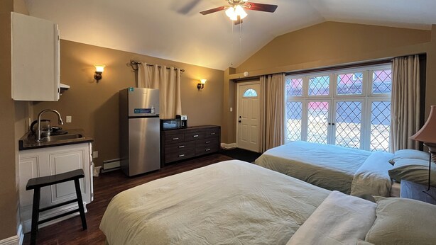 A hotel room with two beds, a kitchenette, a ceiling fan, and a window with a view. -  Cozy room studio (Niagara Falls)
