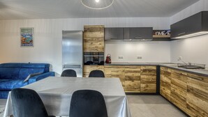A modern kitchen with a wooden island, a dining area with a table and chairs, and a blue sofa. - View Point Semnoz 4* - OG IMMO (Annecy)