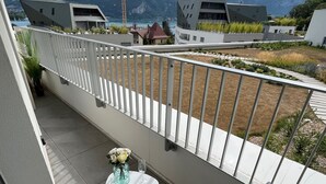 Un balcón con vistas a montañas, una mesa con sillas y un florero con flores.
