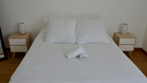 Una cama bien hecha con sábanas blancas, dos mesitas de noche con jarrones decorativos y un suelo de madera.