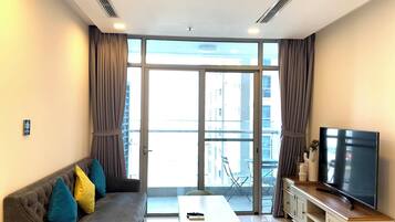 A modern living room with a grey sofa, a coffee table, a TV on a wooden cabinet, and large windows with curtains.