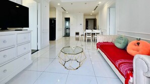 A modern living room with a flat-screen TV, a glass coffee table, a red sofa, and two plush toys. - DongDong LUX APT - Vinhomes Central Park (Ho Chi Minh City)