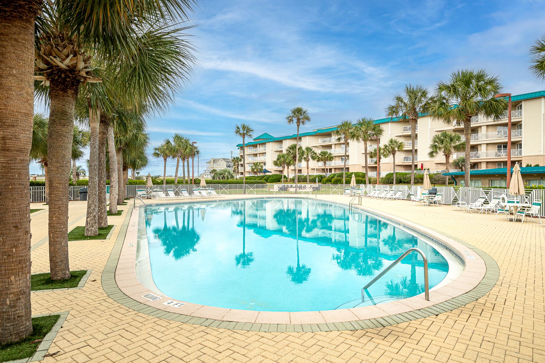 A swimming pool surrounded by palm trees and a hotel building with balconies.