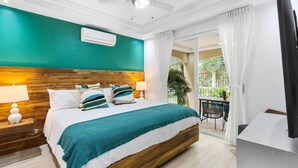 A bedroom with a wooden headboard, a bed with teal bedding, a ceiling fan, and a balcony with a table and chairs. - Stylish Ground floor Condo  walking to Town (Tamarindo)