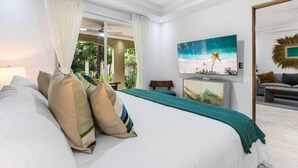 A bedroom with a large bed, a TV, and a view of greenery outside. - Stylish Ground floor Condo  walking to Town (Tamarindo)