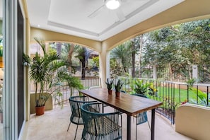 Un patio techado al aire libre con mesa y sillas de madera, rodeado de plantas en macetas y vistas a un jardín exuberante.
