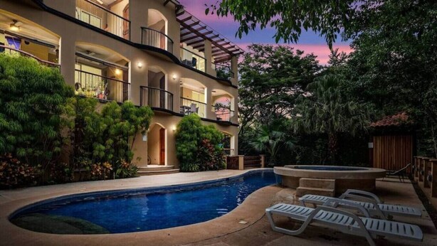 A multi-story building with a swimming pool, outdoor seating, and lush greenery. - Stylish Ground floor Condo  walking to Town (Tamarindo)