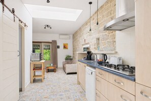 Eine kompakte Küche mit Gaskochfeld, Kaffeemaschine und Spüle. Ein Essbereich mit Tisch und Stühlen lädt zum Verweilen ein, und es bietet sich ein Blick ins Grüne.
