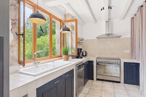 Eine moderne Küche mit großem Fenster, eingebautem Backofen und dunklen Schränken.