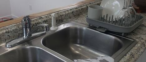 Una cocina con dos lavamanos de acero inoxidable, un escurreplatos y una ventana sobre el lavamanos.