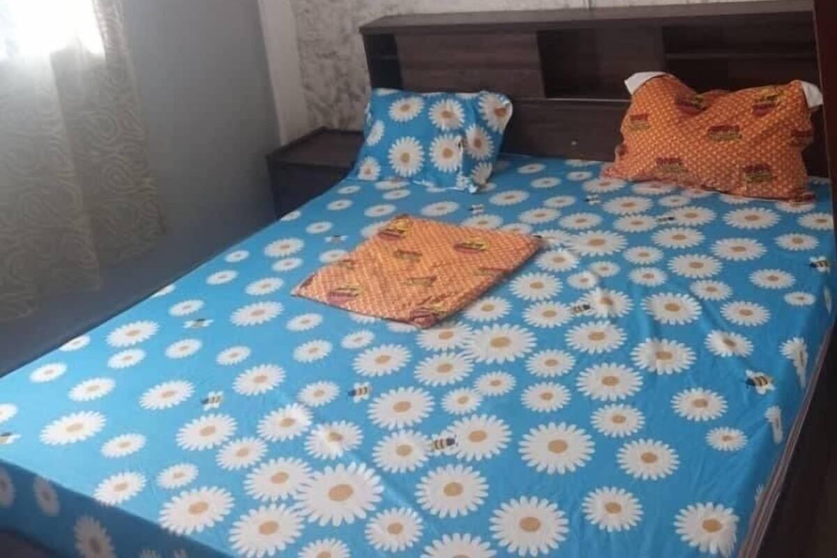 A single bed with a blue and white floral bedspread, two pillows, and a wooden headboard.