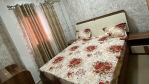 A bedroom with a bed, curtains, a wooden nightstand, and a chair. - LA DIVA (Douala)