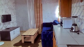 A living room with a blue sofa, a wooden coffee table, a white cabinet, and a ceiling fan. - LA DIVA (Douala)