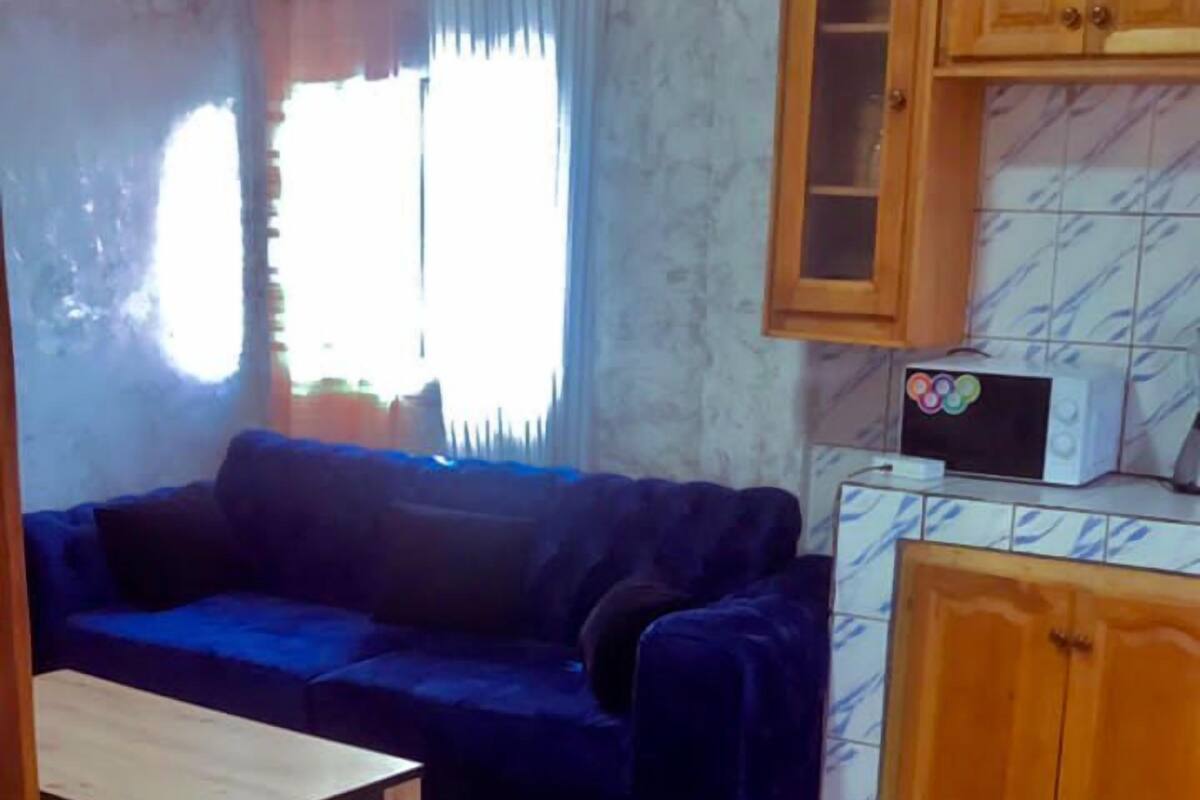 A living room with a blue sofa, a wooden coffee table, a kitchen area with cabinets and a microwave, and a tiled floor.