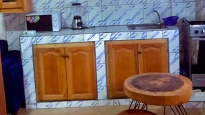 A kitchen with wooden cabinets, a microwave, a sink, and a stove. There is a round wooden table and a rug on the floor. - LA DIVA (Douala)