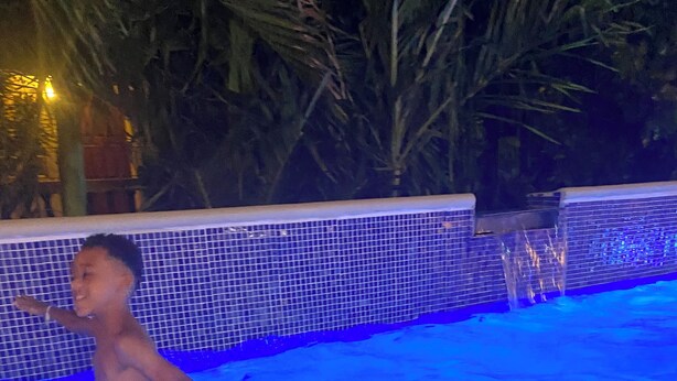 Ein Kind in einem Schwimmbecken mit einer bepflasterten Wand und Wasserspielen.