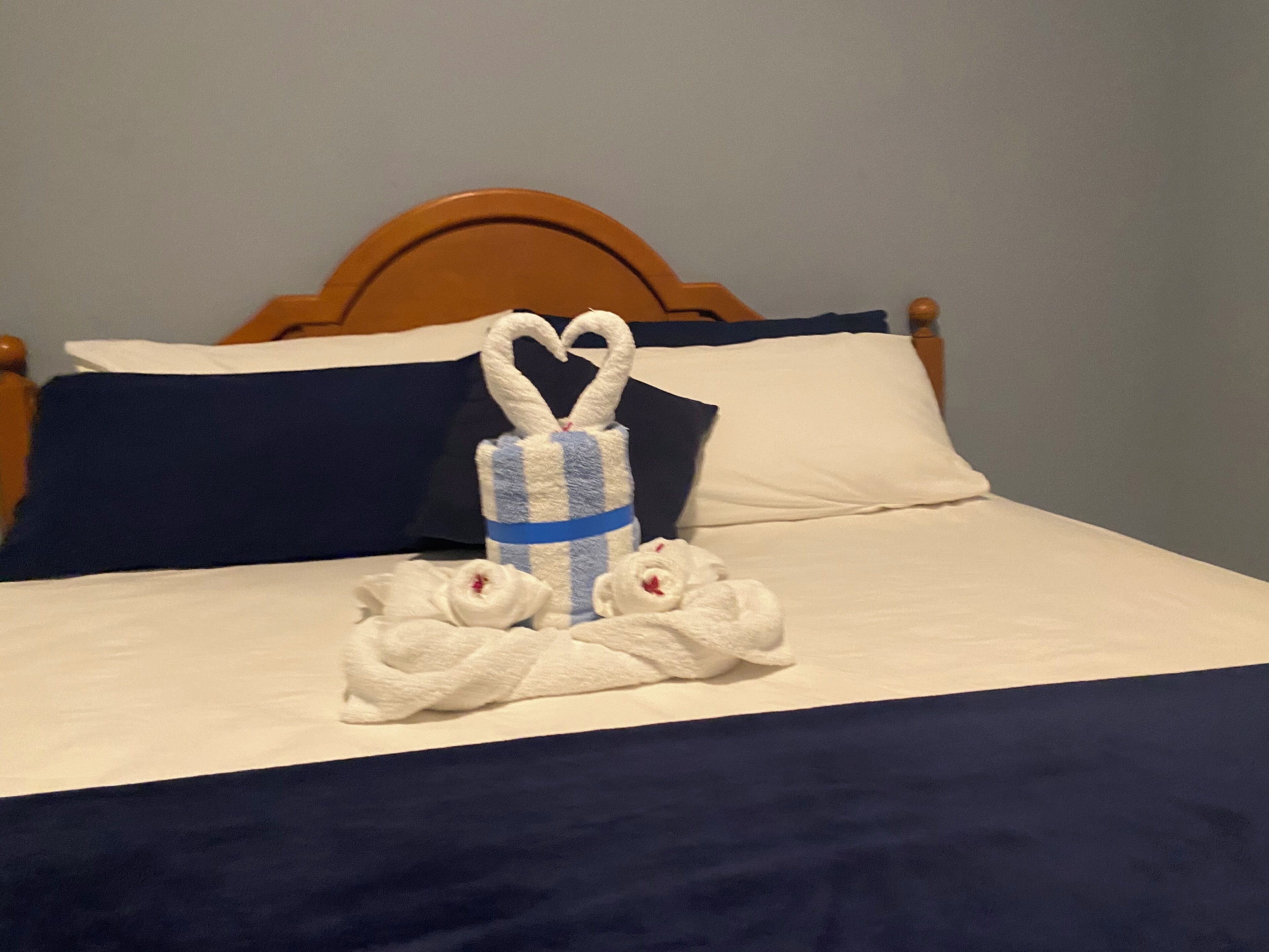 A neatly made bed with a blue and white striped towel and two white towels arranged in a heart shape.