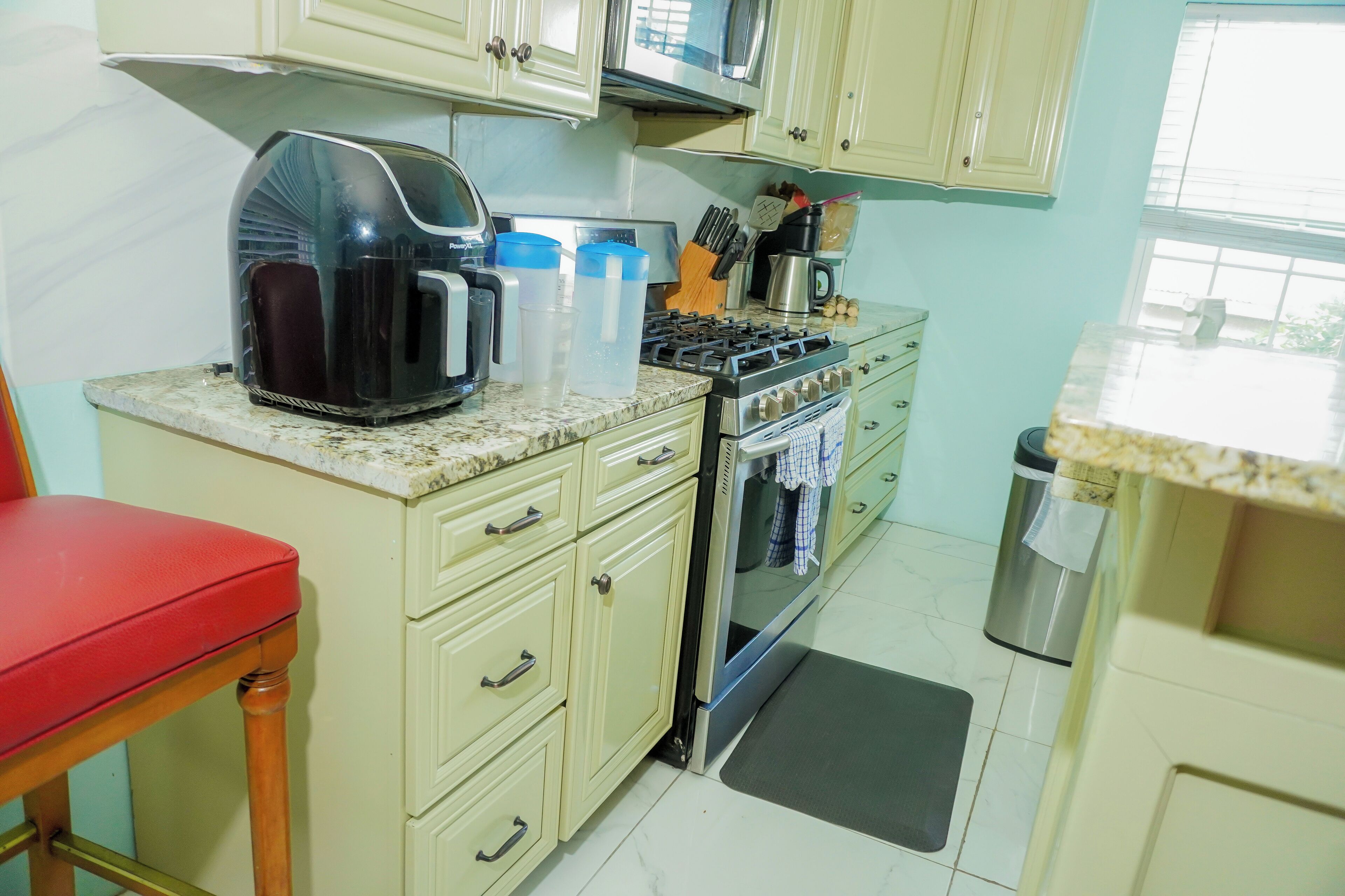 A kitchen with a gas stove, a coffee maker, and a trash can.