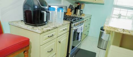 A kitchen with a gas stove, a coffee maker, and a trash can.