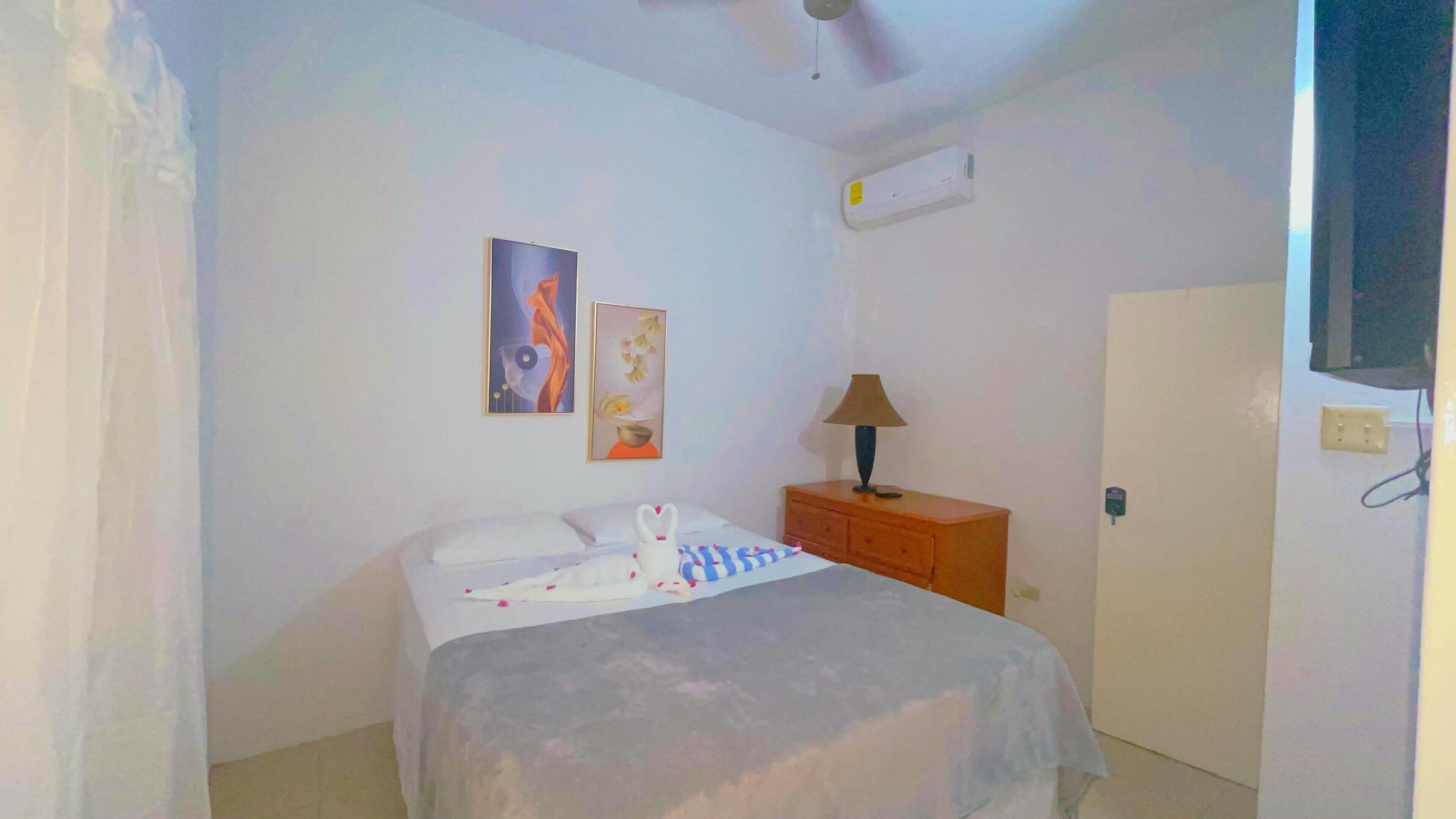 A bedroom with a bed, a nightstand, a lamp, and a wall-mounted air conditioner.