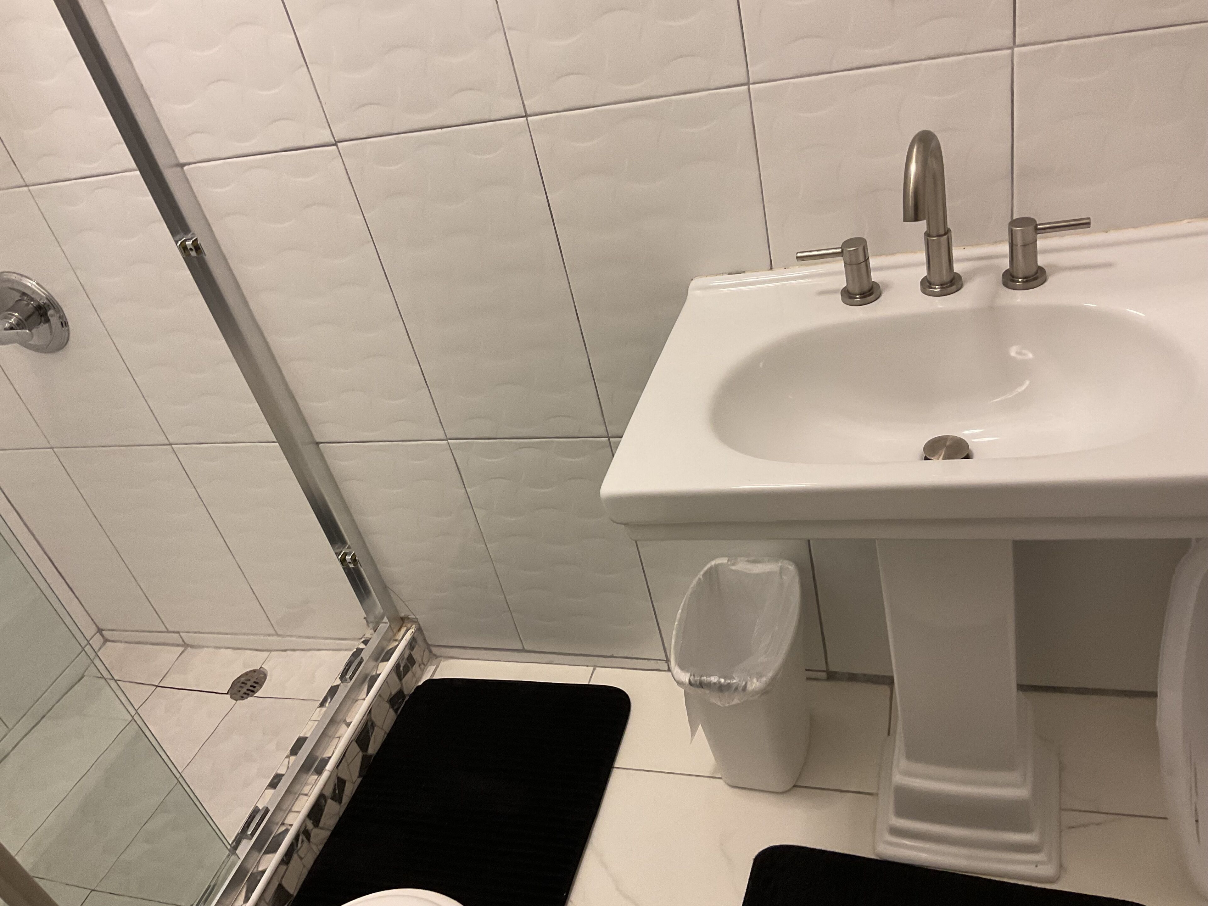 A bathroom with a white sink, a glass shower enclosure, and a black bath mat.