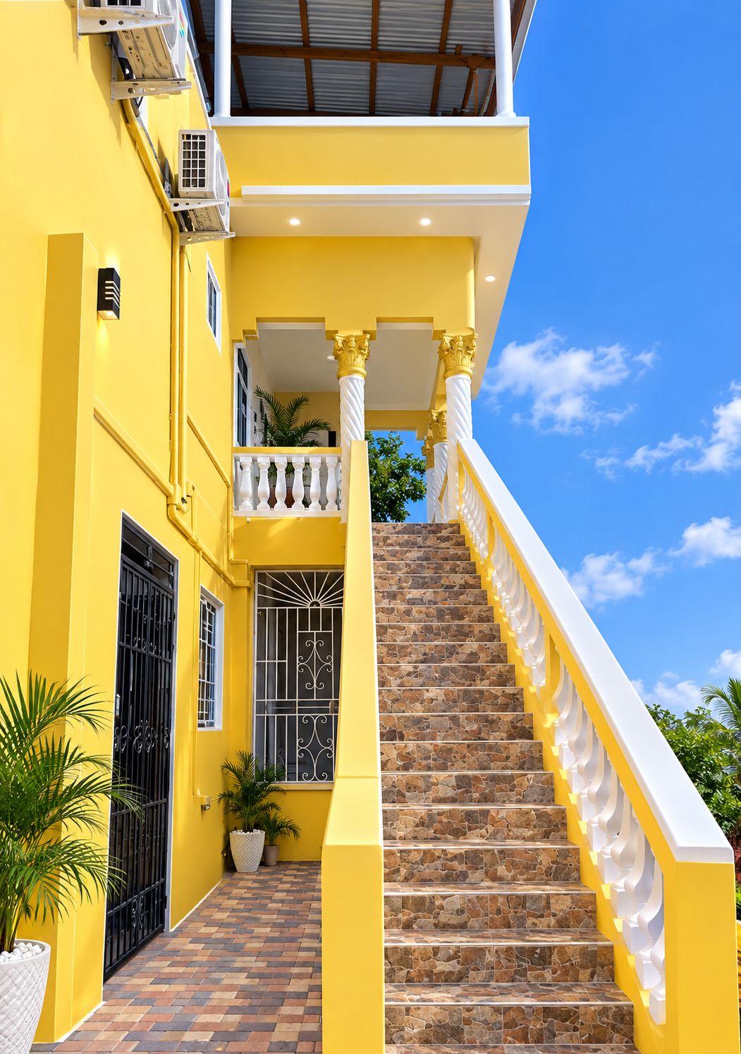 A yellow building with a stone staircase leading to a balcony with white balustrades.