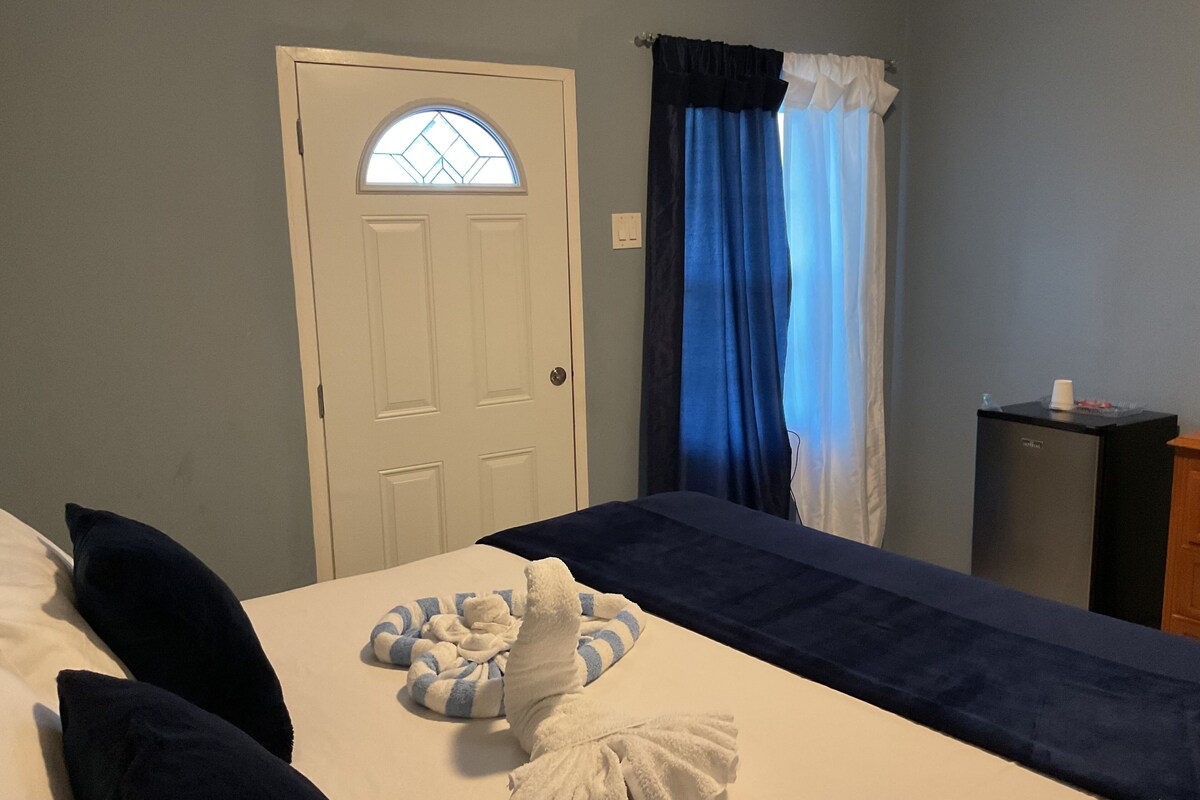 A hotel room with a bed, a small desk, a window with curtains, and a door with a glass panel.