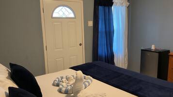 A hotel room with a bed, a small desk, a window with curtains, and a door with a glass panel.