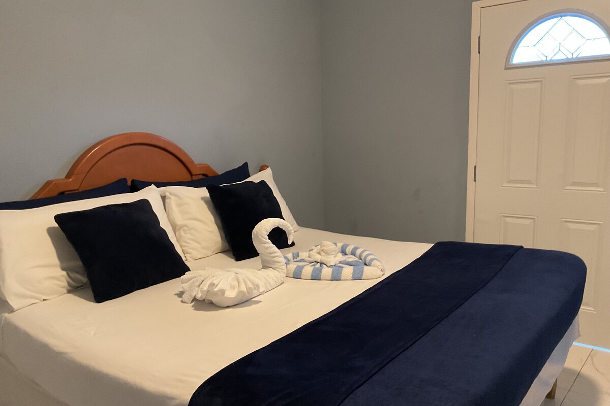 A neatly made bed with a blue and white striped blanket, a white swan-shaped pillow, and navy blue pillows.