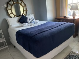 Una cama bien hecha con una manta azul, almohadas blancas y un cabecero decorativo.